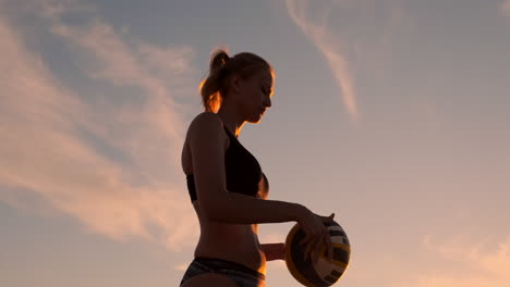 A-beautiful-woman-in-a-bikini-with-a-ball-at-sunset-is-getting-ready-to-do-serve-jump-on-the-beach-in-a-volleyball-match-on-the-sand.-The-decisive-moment-the-tense-moment-of-the-match-in-slow-motion.